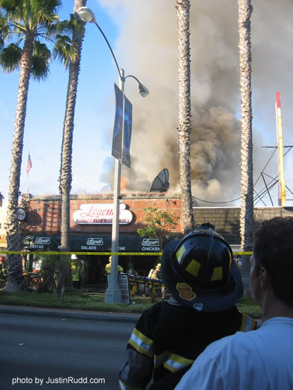 A youngster dressed as a fireman and being held tightly by his father watches the burning building from across 2nd St.