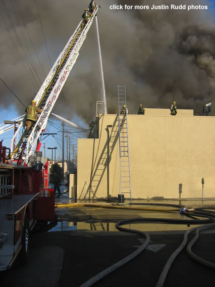 As seen from the parking lot of Jack in the Box, firefighters climb ladders to tackle the fire and its smoke.