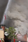 The American Flag stands tall as billows of smoke rise during the downpour as a fire hose douses the burning building. (44kb)