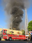 As blue skies look on, Ladder Truck T17 pumps water onto the flames of the burning building. (50kb)