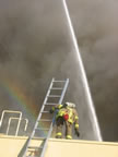 A rainbow of hope (bottom left) brings a bit of hope as a fireman looks on, while a ladder truck forcefully shoots tons of water down onto the burning building. (26kb)