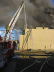 As seen from the parking lot of Jack in the Box, firefighters climb ladders to tackle the fire and its smoke. (44kb)